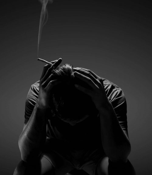 Depressed man smoking cigarette sitting on chair on black background